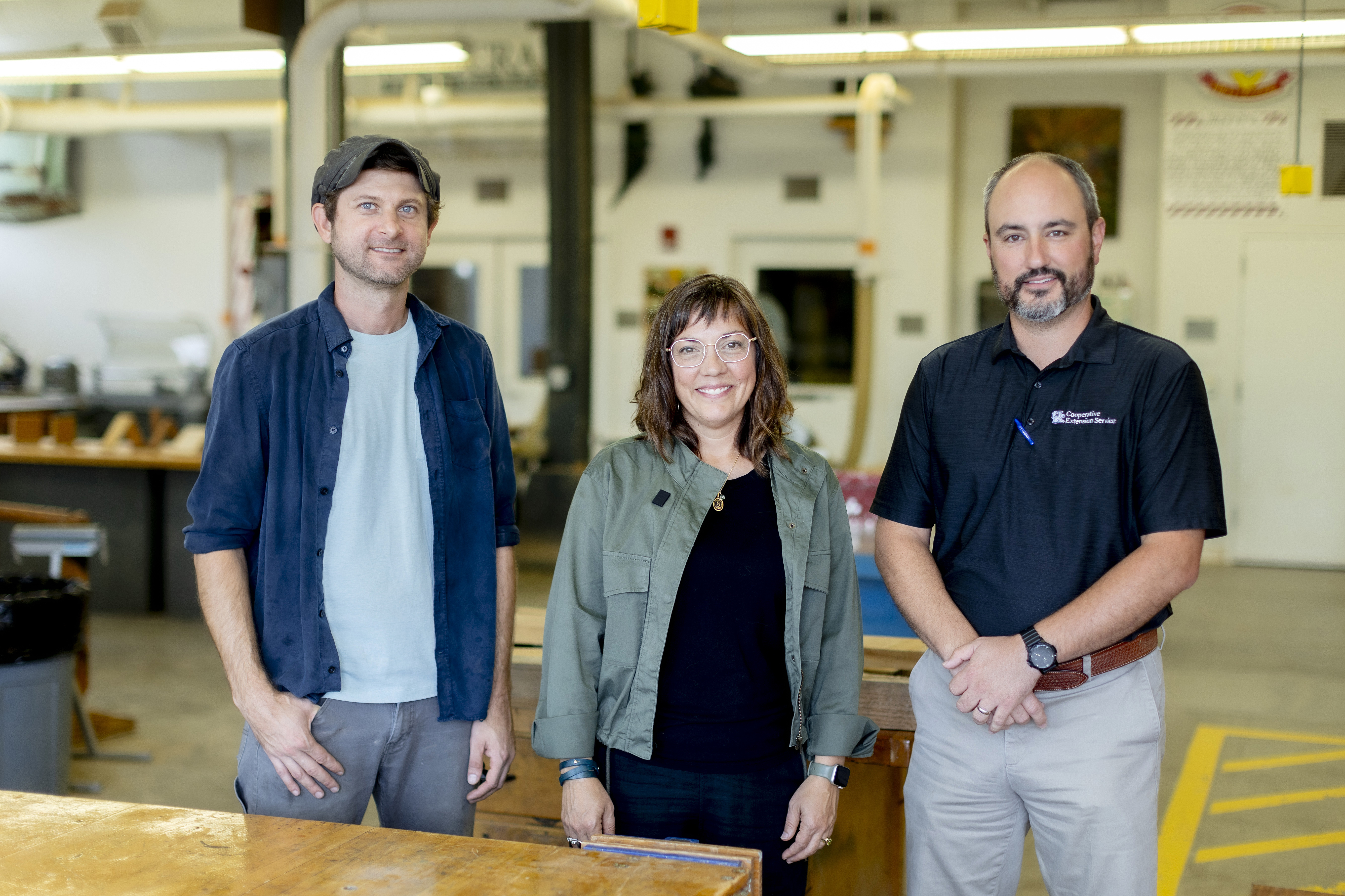Two men and one woman pose for a photo in a woodworking shop