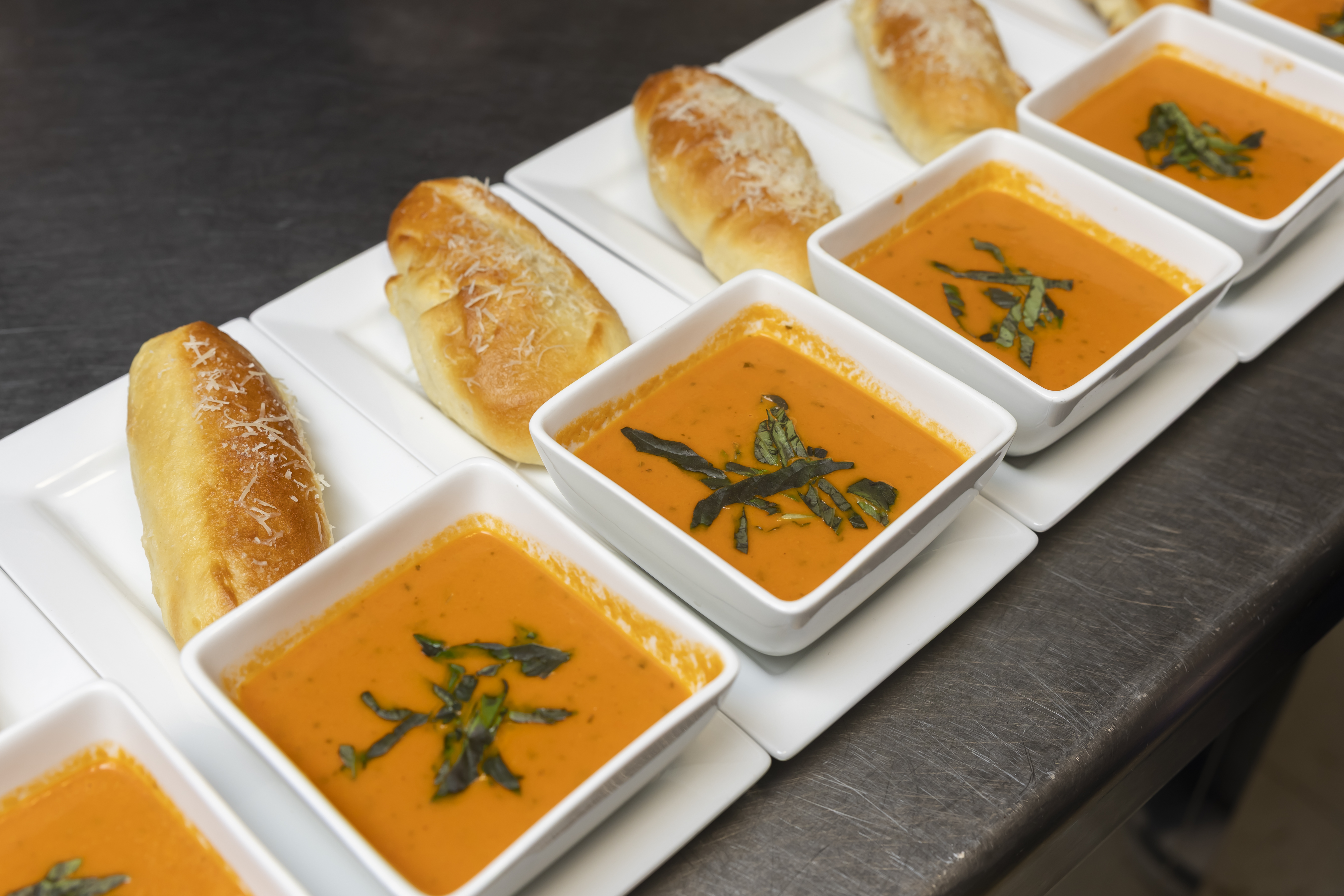 A view of several prepared plates of orange-colored soup and loaves of bread. 