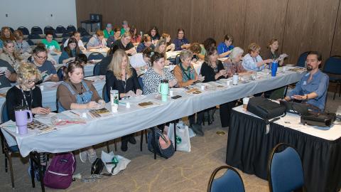 Volunteers in a demonstration class with several materials on tables. 
